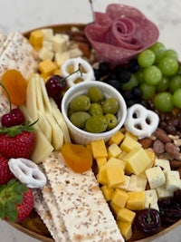 a wooden platter with a variety of cheeses, fruits and crackers