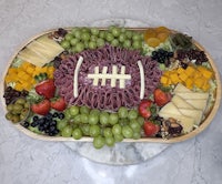 a football shaped tray with cheese, fruit and grapes